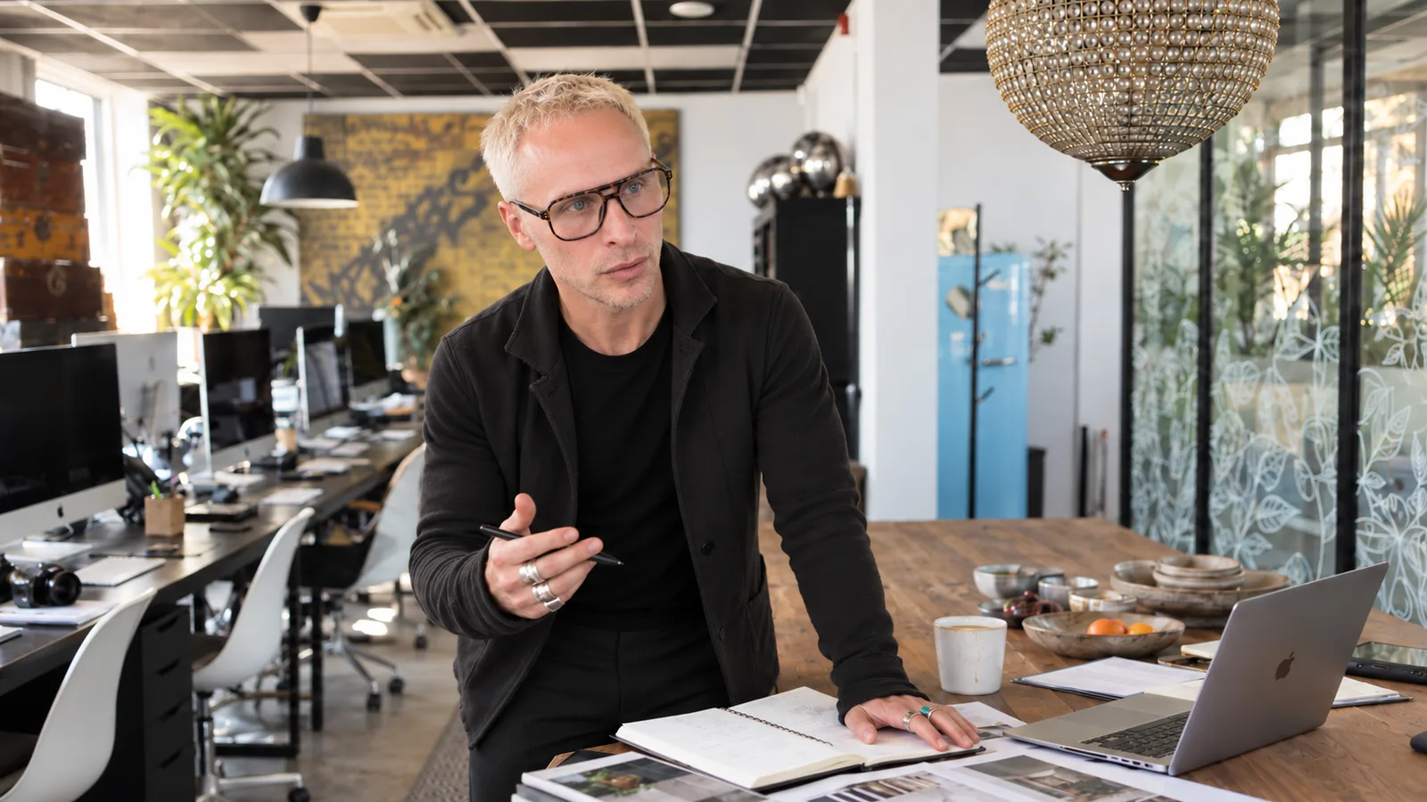Samuel Collett at the studio table, mid-conversation, with notebooks and a laptop.
