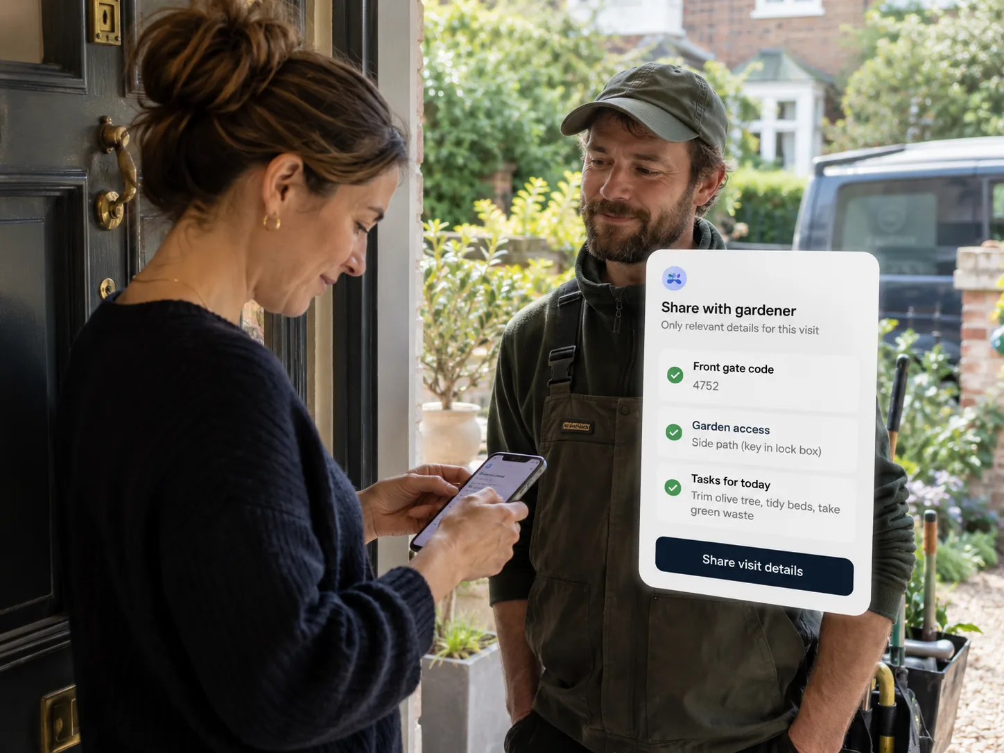 A woman at her front door sharing visit details from her phone with a gardener.